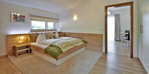 Quarto com cama, mesas de cabeceira, janela e vista para uma sala de jantar.
