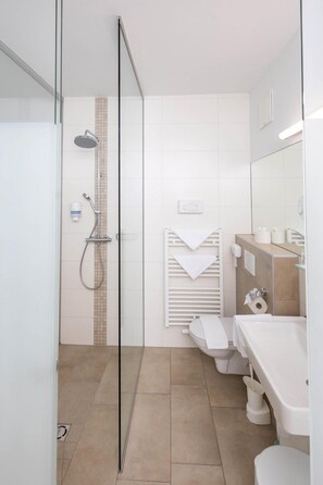 Un baño moderno con cabina de ducha de vidrio, un lavamanos blanco y un inodoro.