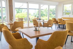 Un comedor moderno con ventanas amplias, sillas amarillas y una mesa de madera con saleros y pimenteros.