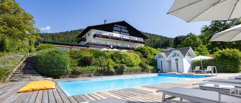 A hotel with a pool, wooden deck, and lounge chairs.