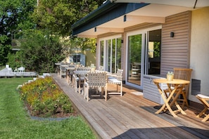 Un patio techado al aire libre con mobiliario de madera y vistas a la casa.