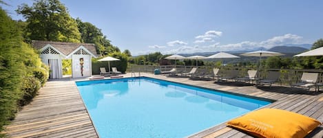 A swimming pool with a wooden deck, lounge chairs, and umbrellas.