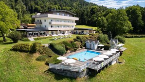 Un hotel de varios pisos con piscina, zona de estar al aire libre y vistas a una ladera boscosa.