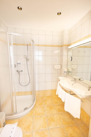 Un baño con ducha envuelta en vidrio, lavamanos con espejo y un perchero para toallas.