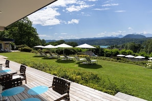 Una terraza con asientos exteriores y sombrillas, con vista a un área verde y montañas al fondo.