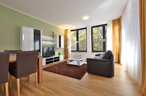 A modern living room with a flat-screen TV, a sofa, a coffee table, and a dining area with chairs. - Business Suiten (Munich)