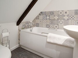 Un baño con una bañera independiente, un lavamanos blanco y un salpicadero de azulejos estampados.