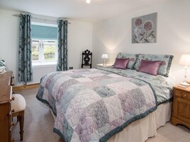 Un dormitorio con cama, mesita de noche, una silla, una ventana con cortinas y una lámpara de pared.