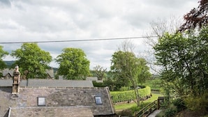 A stone-roofed building with a garden view, a wooden fence, and a patio table with chairs. - Chatton Cottage (Alnwick)