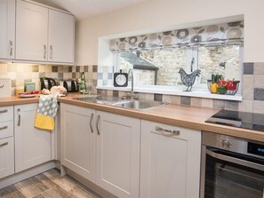A kitchen with a stone wall, a window with a view, a sink, and a stove. - Chatton Cottage (Alnwick)