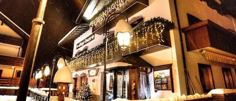 A snow-covered outdoor area with a building featuring a balcony and a sign that reads 'Hotel'.