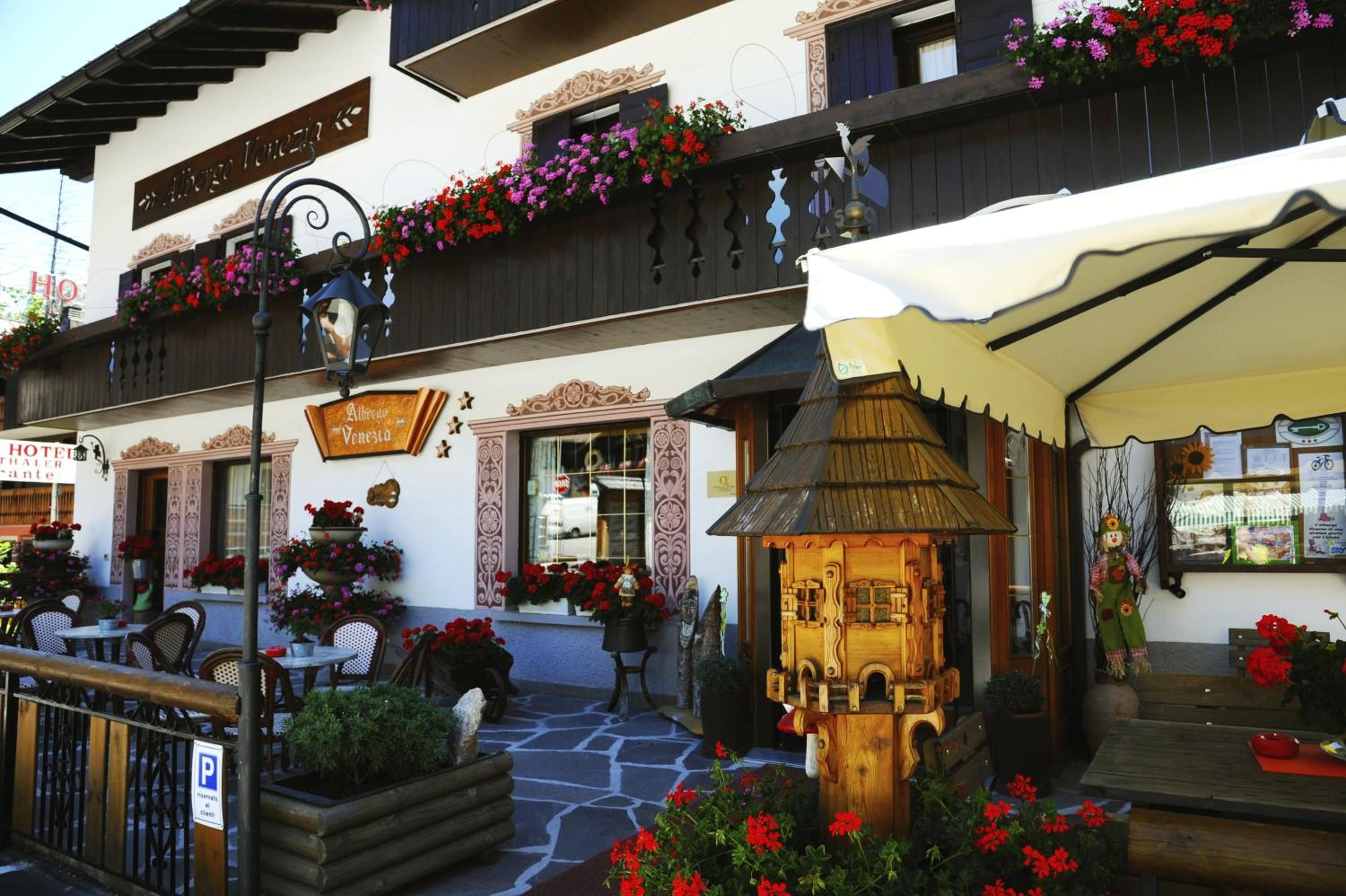 A traditional European hotel with outdoor seating, flower arrangements, and a wooden lantern.