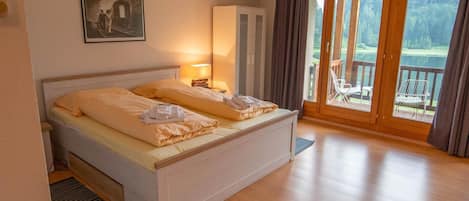 Habitación de hotel con cama, lámpara de noche, armario y una ventana grande con vistas a una terraza y árboles.