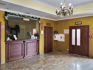 A hotel reception area with a reception desk, a chandelier, and two doors labeled 'HOTEL' and 'RECEPTION'.