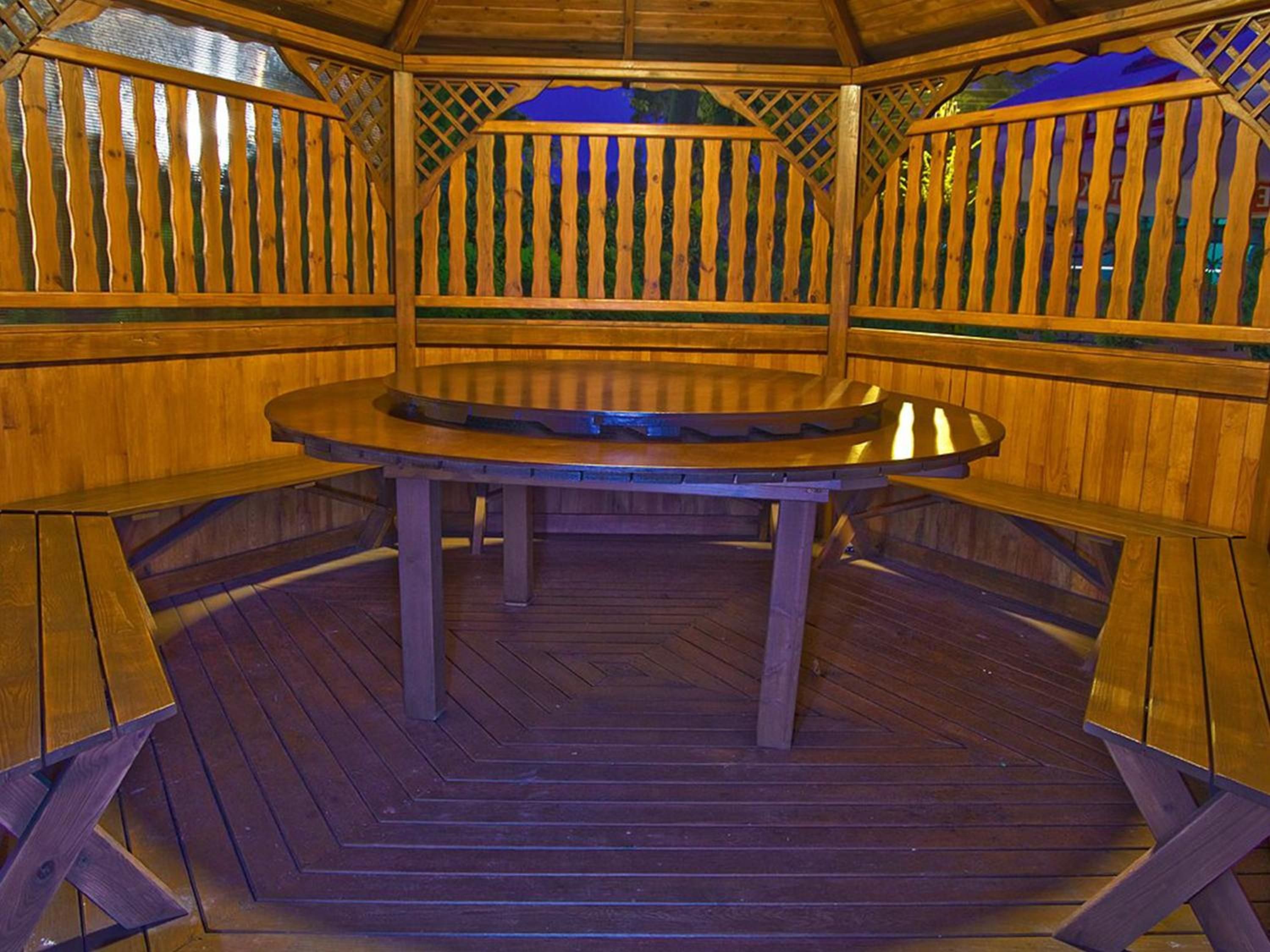 A wooden gazebo with a round table and benches.