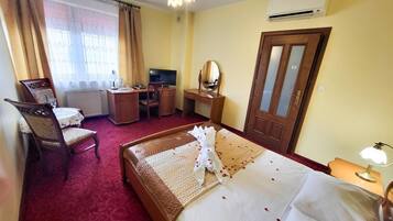 A hotel room with a bed, a desk, a chair, a television, and an air conditioning unit.