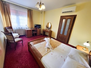 A hotel room with a bed, a desk, a chair, a television, and an air conditioning unit.