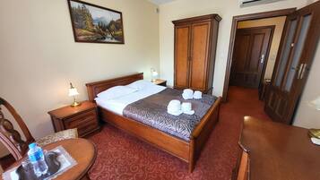 A hotel room with a bed, a desk, a chair, a wardrobe, and an air conditioning unit.