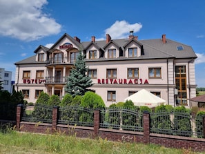 A hotel with a restaurant on the ground floor, multiple balconies, and a well-maintained garden.
