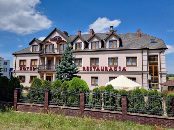 A hotel with a restaurant on the ground floor, multiple balconies, and a well-maintained garden.