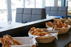 Zona de buffet con pan y pasteles en cestas, una barra y asientos.