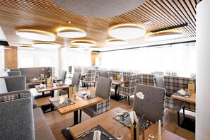Interior de restaurante moderno con techos altos de madera, luminarias circulares y una combinación de cabinas y mesas tapizadas en gris.