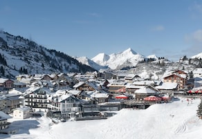 Un pueblo cubierto de nieve en la montaña, con edificios y una pista de esquí.