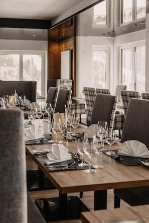 Comedor con varias mesas dispuestas para una comida, sillas y vistas al exterior a través de amplios ventanales.