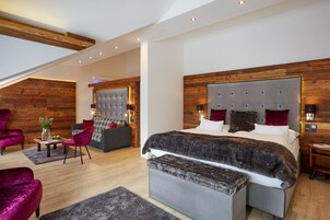 Un dormitorio moderno con una cama grande, una zona de estar con sofá y sillones, y un techo de madera.