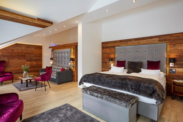 Un dormitorio moderno con una cama grande, una zona de estar con sofá y sillones, y un techo de madera.