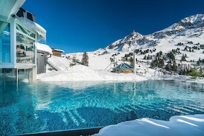 Una piscina con agua azul cristalina, rodeada de nieve y montañas.
