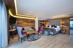Habitación de hotel moderna con un muro de acento de madera, un sofá, una silla, una cama y un escritorio con una lámpara.