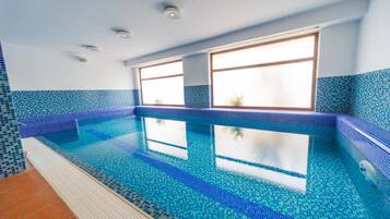A swimming pool with clear blue water, surrounded by blue-tiled walls and a window with a view.
