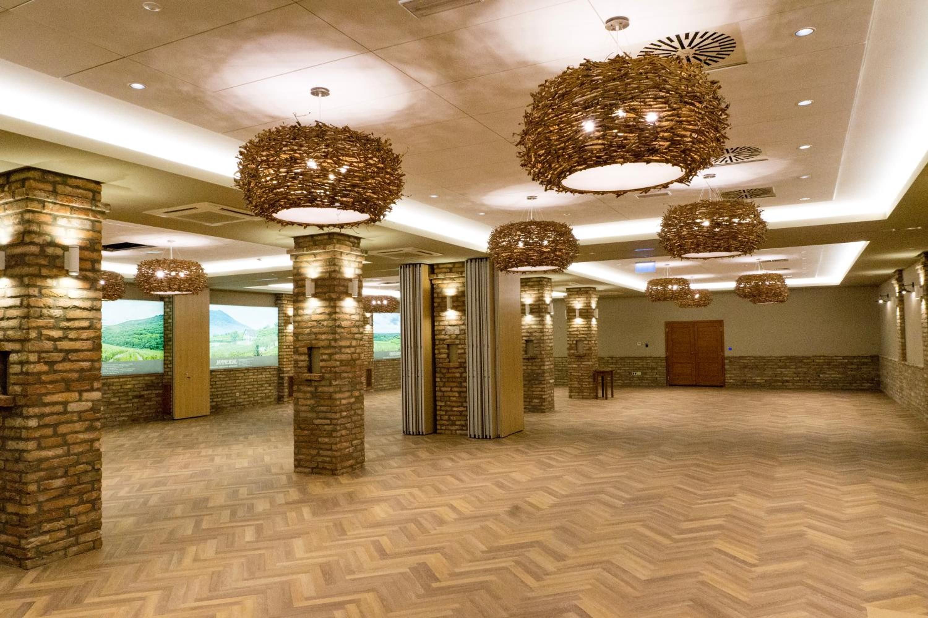 A spacious hotel lobby with high ceilings, stone pillars, and hanging wicker chandeliers.
