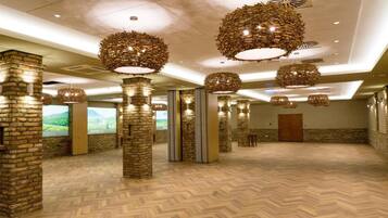 A spacious hotel lobby with high ceilings, stone pillars, and hanging wicker chandeliers.