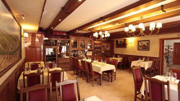 A restaurant interior with wooden beams, chandeliers, and tables set for dining.