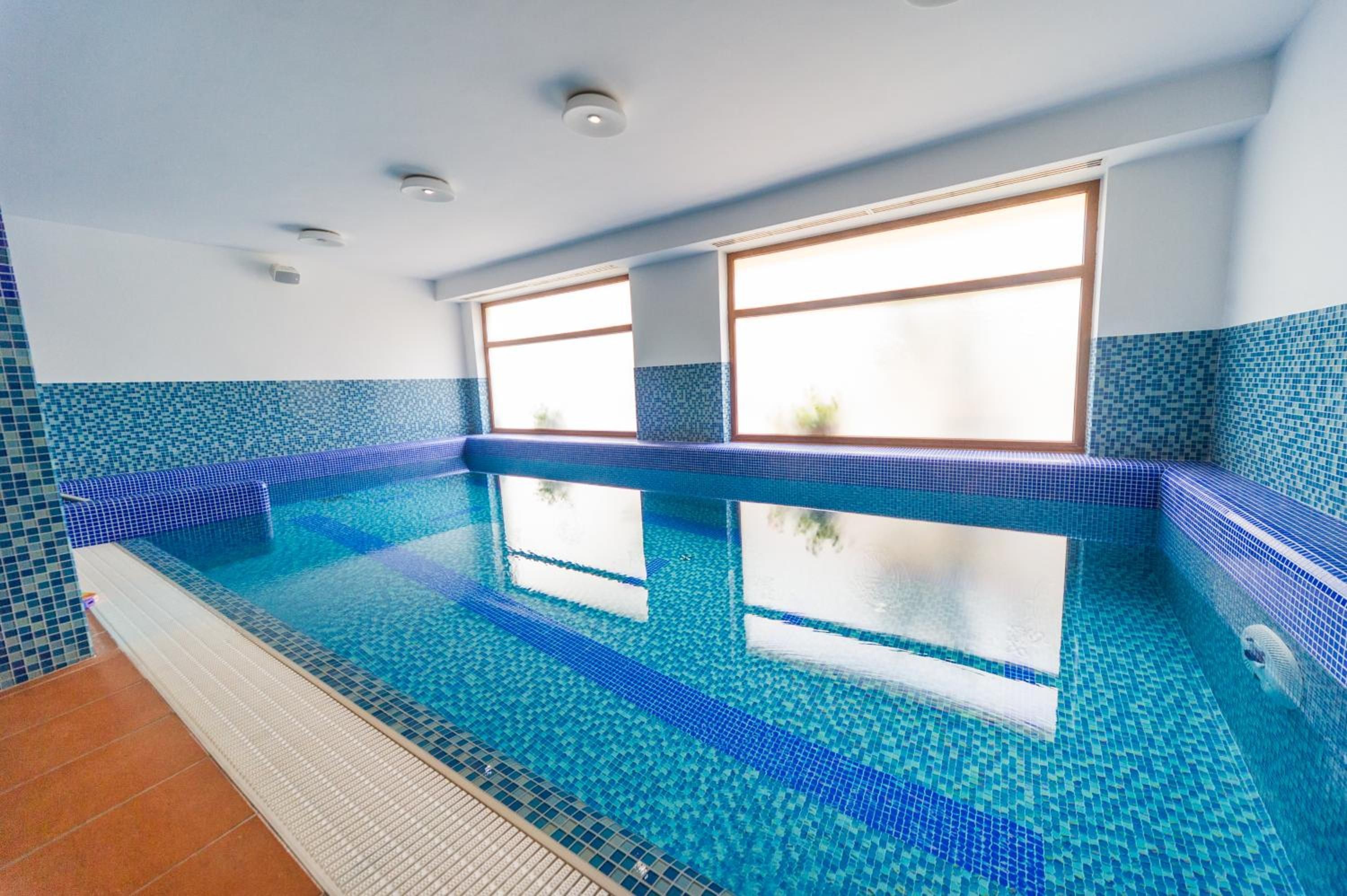 A swimming pool with clear blue water, surrounded by blue-tiled walls and a window with a view.