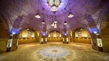 A spacious hall with a circular mosaic floor, arched brick walls, and hanging pendant lights.