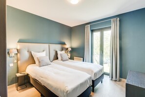 Un dormitorio moderno con dos camas, una mesita de noche, un escritorio y un amplio ventanal con cortinas.