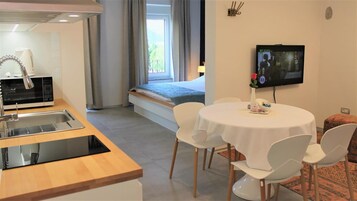 A hotel room with a kitchenette, a dining area with a table and chairs, a television, and a bed with a view of the outdoors.