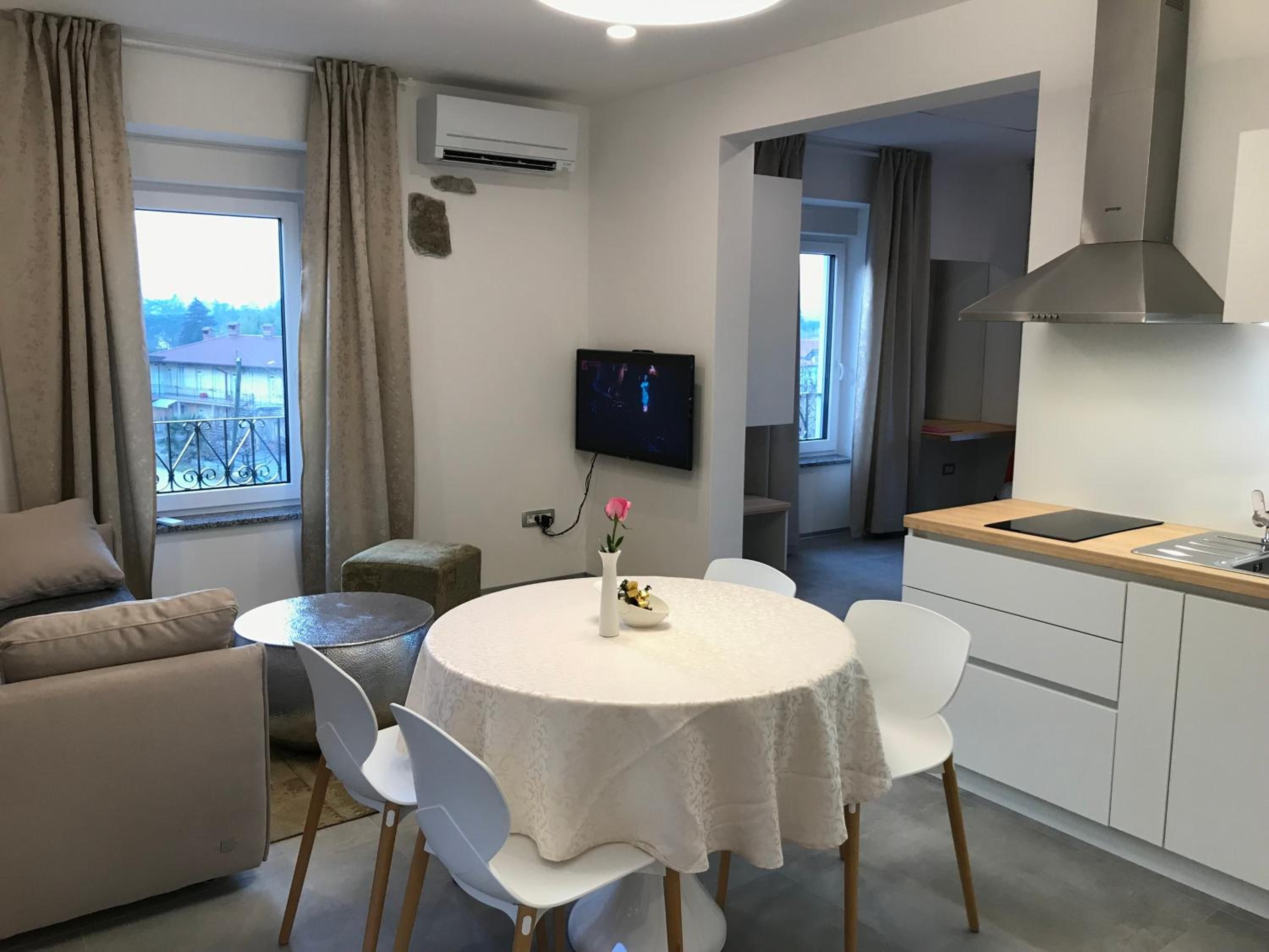 Un espace de vie moderne comprenant une table à manger ronde, des chaises blanches, un canapé, un téléviseur fixé au mur et un coin cuisine avec un plan de travail et des placards.