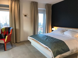Habitación de hotel con cama, una silla, un ventanal y vistas al exterior.