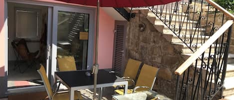 Zona esterna con posti a sedere, un tavolo, sedie, un ombrello rosso e una scala con gradini in pietra.