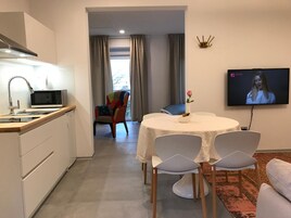Cocina moderna con microondas, lavamanos y una silla. Hay una zona de comedor con una mesa y sillas, y un televisor montado en la pared.