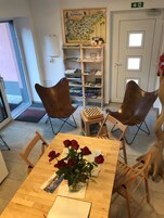 Una habitación con una mesa de madera, dos sillones de cuero, un pequeño tablero de ajedrez, un florero con rosas rojas, una estantería llena de libros y un mapa en la pared.