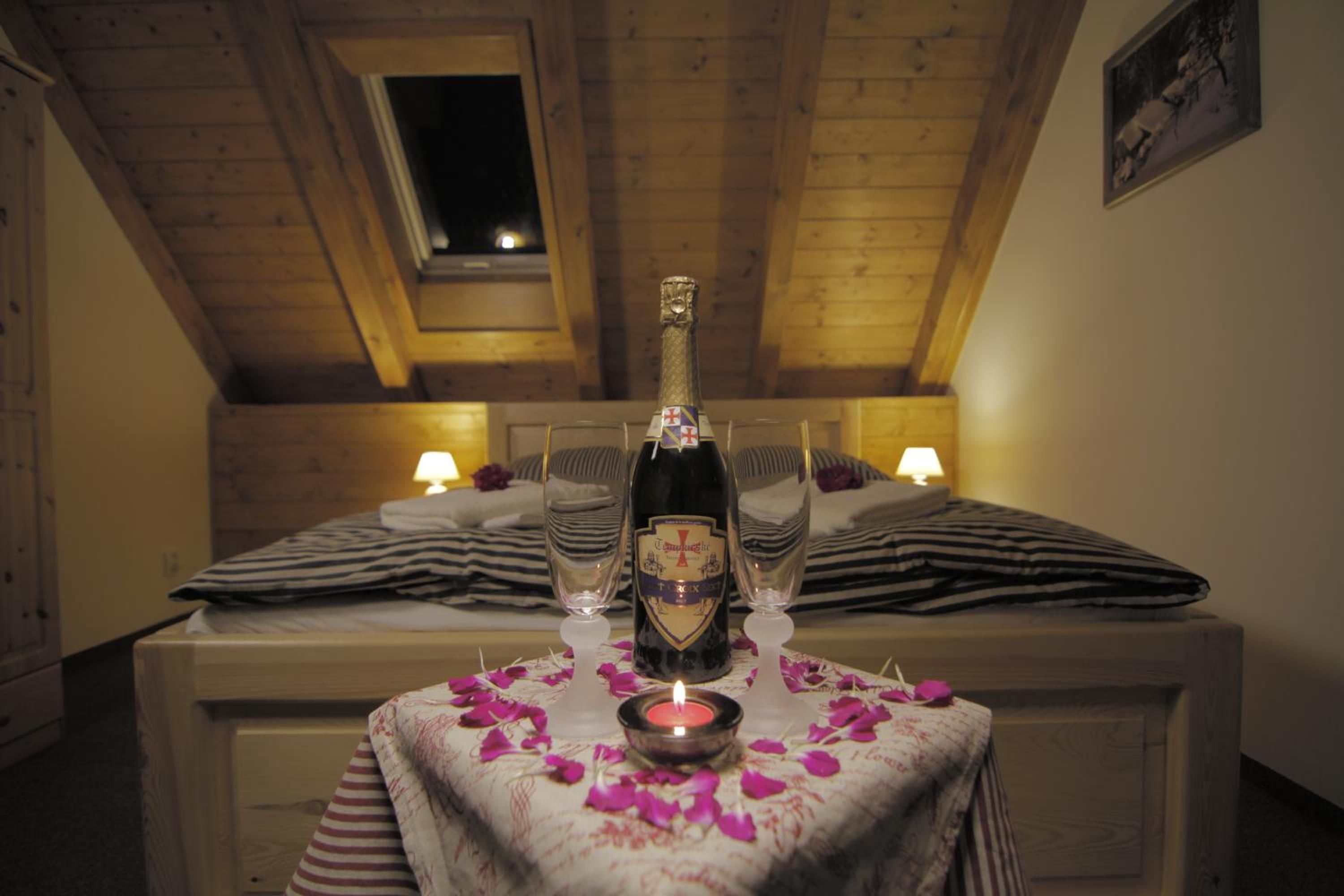 A cozy room with a wooden ceiling, a bed with striped bedding, a table with a bottle and glasses, and a lit candle.