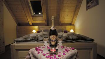 A cozy room with a wooden ceiling, a bed with striped bedding, a table with a bottle and glasses, and a lit candle.