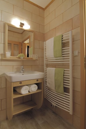 A bathroom with a sink, mirror, towel rack, and a wooden shelf with towels. - Pension U Lipy (Arnoltice)