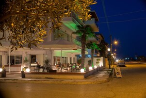 Hotel con terraza al aire libre, una palmera y vista a la calle de noche.