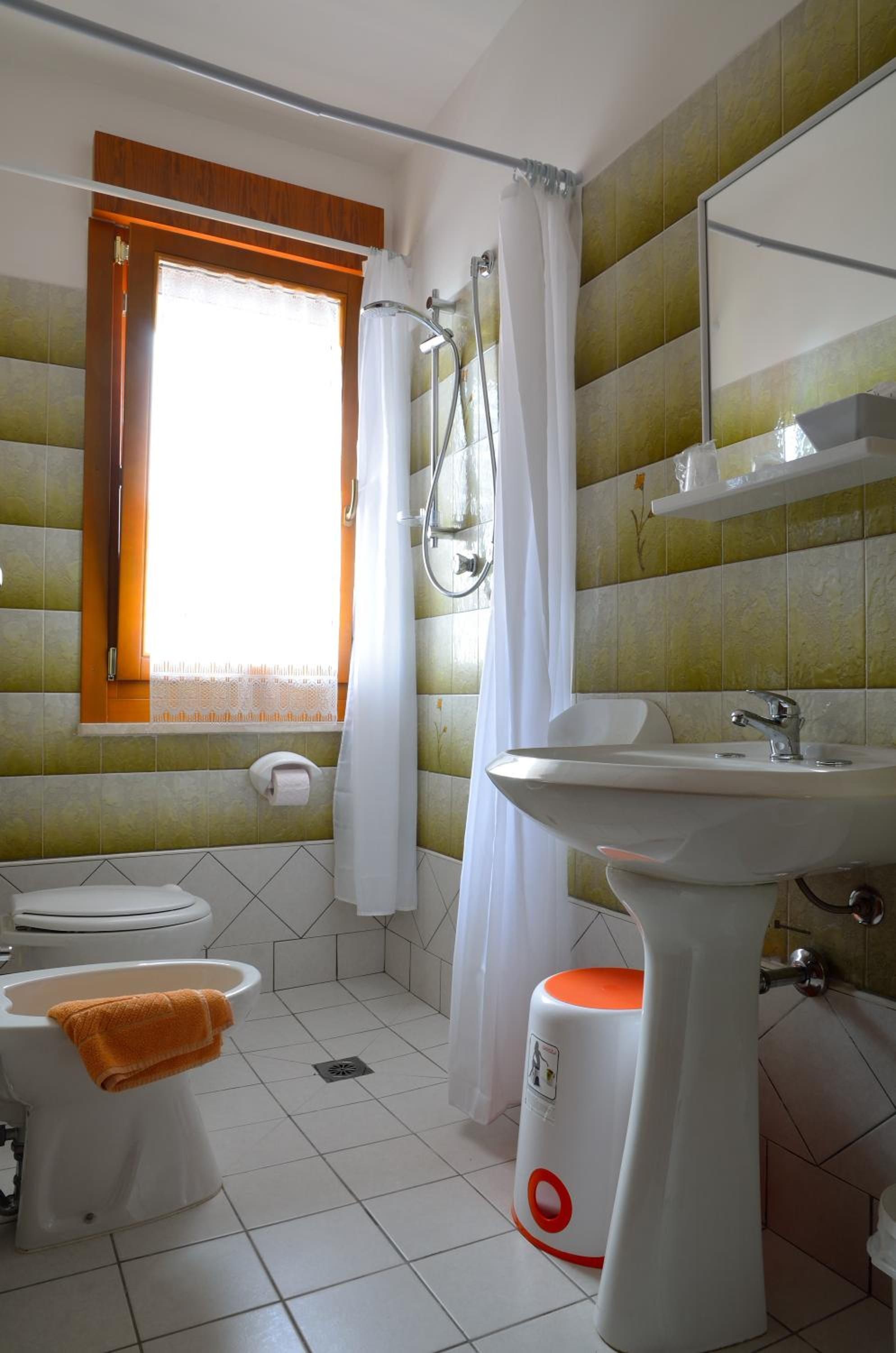 Un baño con inodoro, lavamanos, ducha y ventana con cortinas.